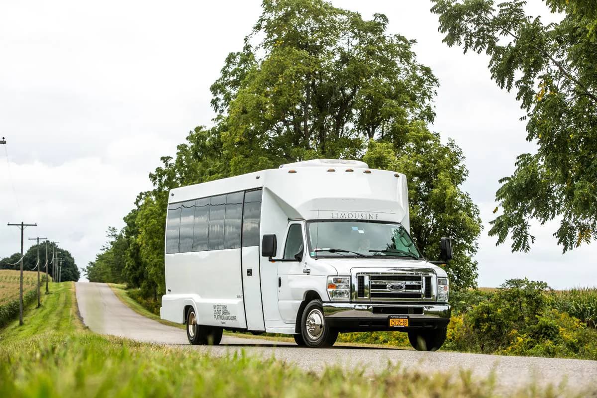 White limo bus parked on a road with trees in the background